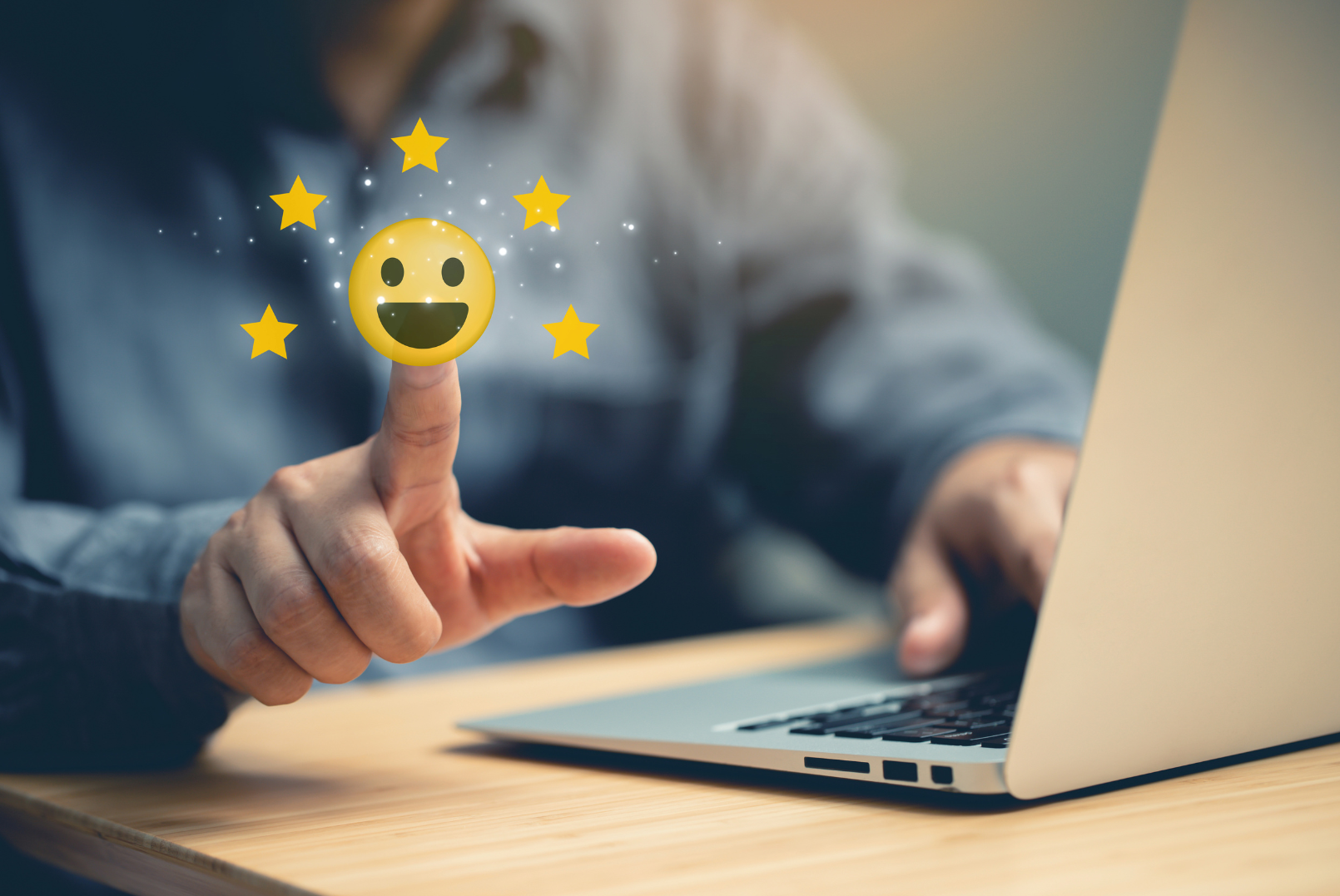 A person sitting in front of a laptop, hand touching a smiley face with 5 stars around it.