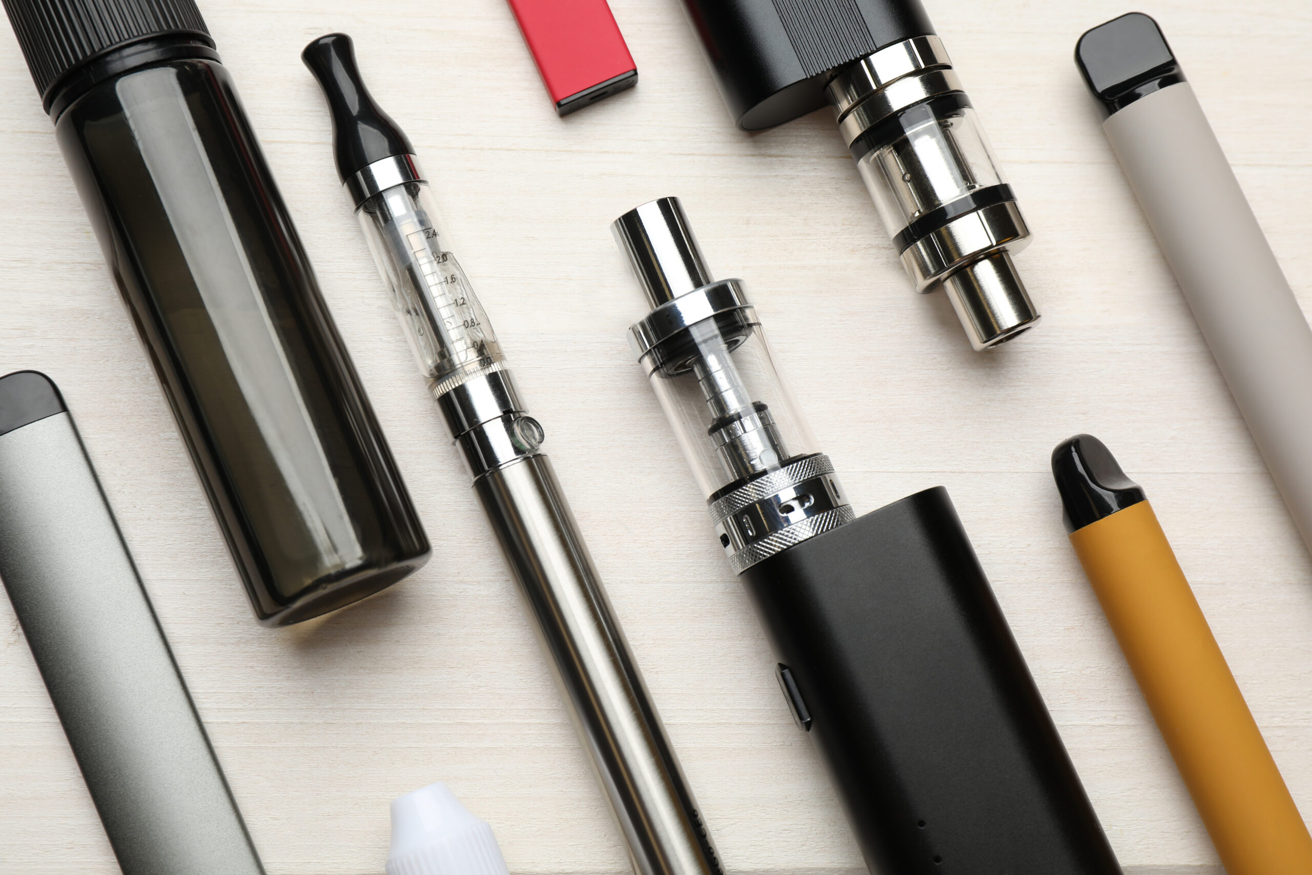 Different electronic cigarettes on white wooden table, flat lay.